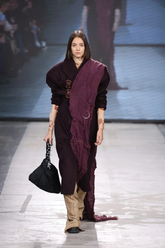 modella che sfila con indosso un vestito color prugna