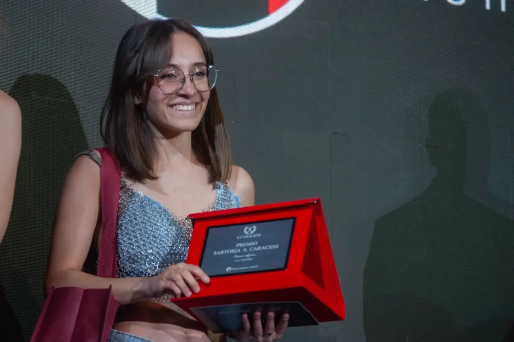 studentessa che sorride con in mano una targa rossa con un premio