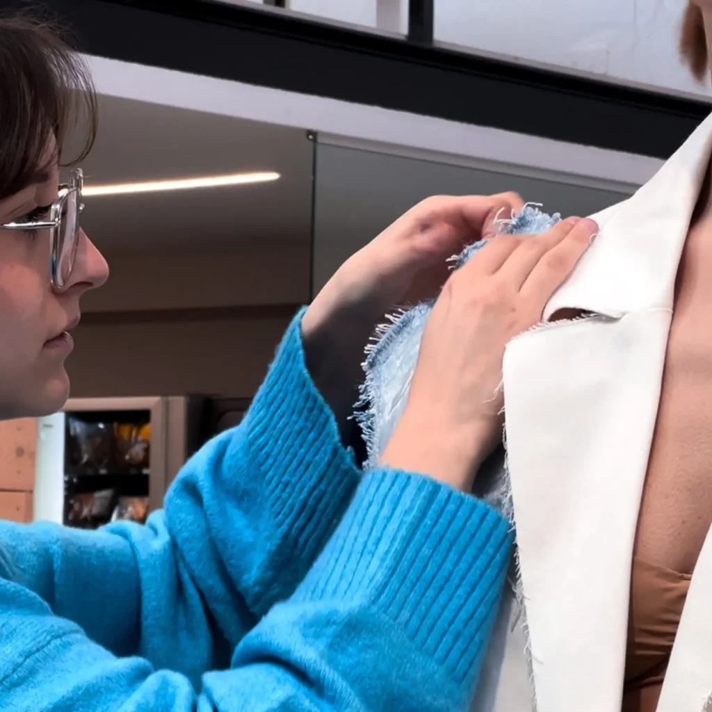 una studentessa che con uno spillo sistema gli ultimi ritocchi di un blazer indosso a un modello.