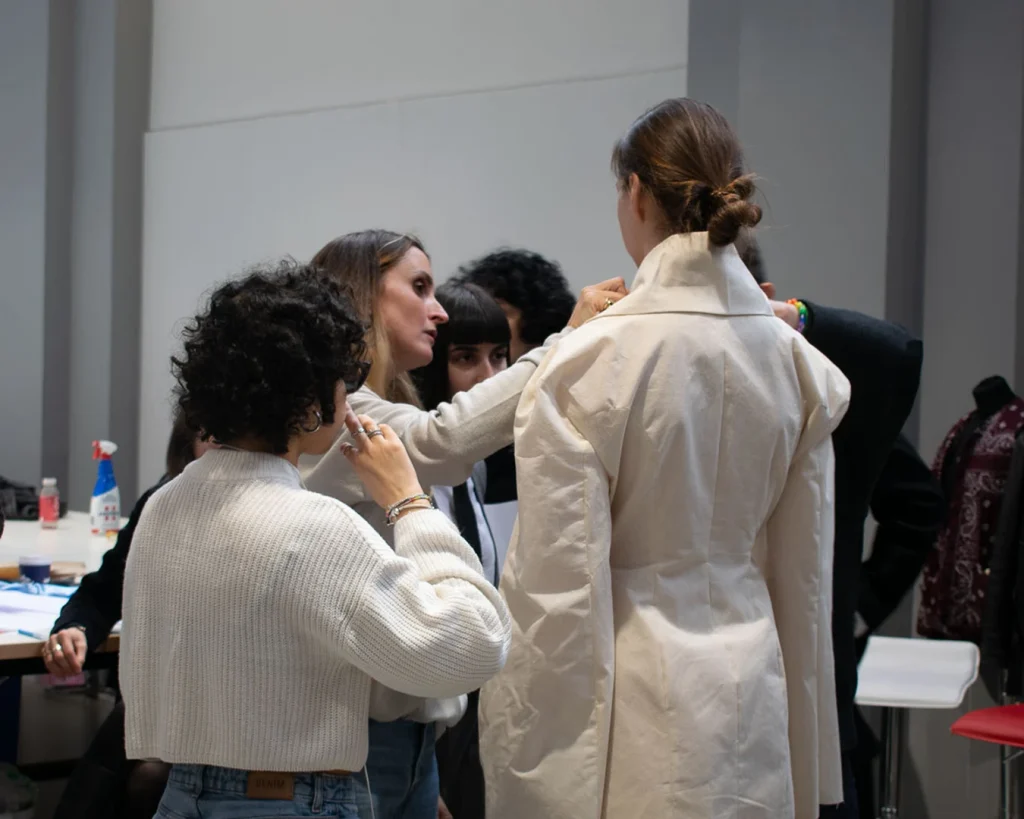 Studenti di moda lavorano su un capo bianco indossato da una modella in aula di laboratorio.
