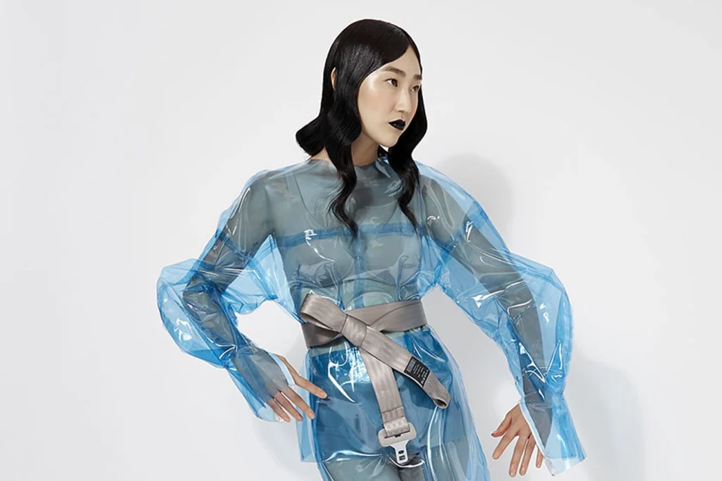 Modella in posa su sfondo bianco indossa un abito di plastica trasparente azzurro.