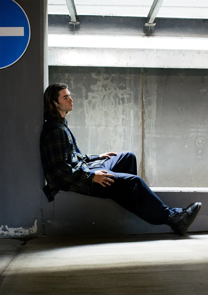Model sitting in a parking lot wearing shirt and trousers made by students.